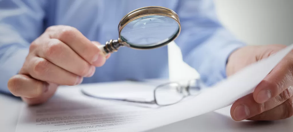 Адвокат з перевірок бізнеса Чоловік в білій сорочці крізь лупу уважно вивчає документ - Адвокат з перевірок бізнеса