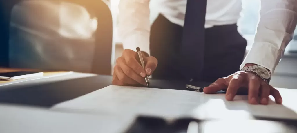 Кримінальний адвокат Кримінальний адвокат у краватці, без піджака, стоячі з ручкою за столом аналізує справу