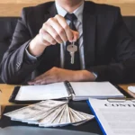 Людина в костюмі, з ключем, моделлю будинку, контрактом і грошима на столі - символізує забезпечення виконання договорів