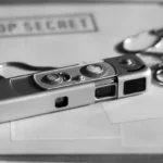 Шпигунський фотоапарат лежить на стосі паперів із написом «ЦІЛКОМ ТАЄМНО» - комерційна таємниця під загрозою